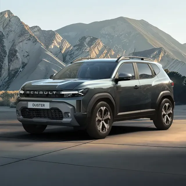 Front three-quarter view of a silver Renault Duster SUV on a mountain road with rugged peaks in the background.