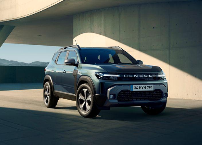 Front three-quarter view of a blue Renault SUV parked on a concrete plaza under a curved architectural structure, daytime light.