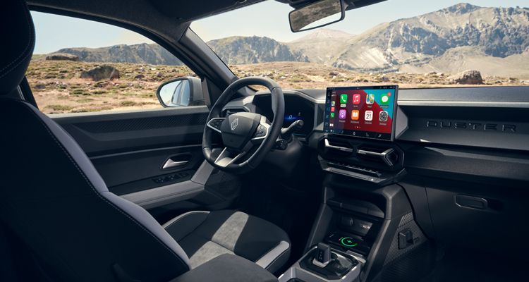 Interior of a modern car with a steering wheel and large infotainment touchscreen, mountains visible outside.
