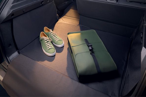 Green backpack or duffel bag with a strap sits on the right side of a car's back seat, next to a pair of green sneakers with white soles.