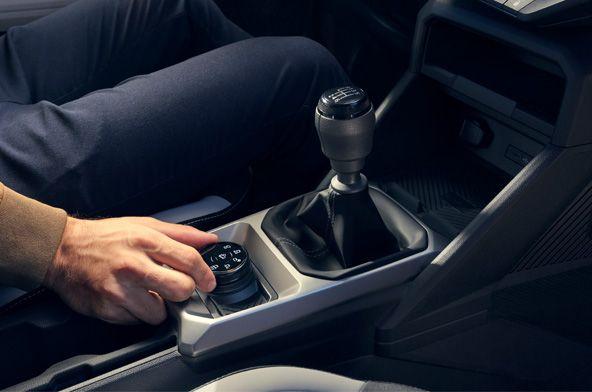 Person's hand turning a control knob on the center console beside the manual gear stick in a car interior