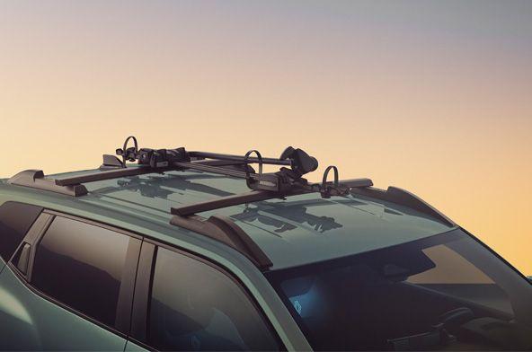 Teal SUV with a roof rack and bike carriers attached, seen from the side at sunset.