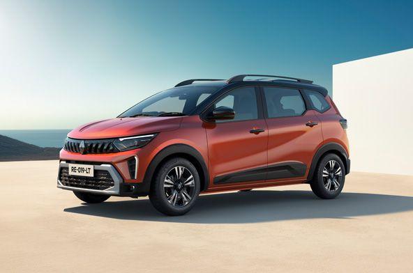 Orange crossover SUV parked on a sunny coastal plaza, front three-quarter view showing black roof rails and alloy wheels on a clear day with sea in the background