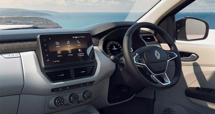 Interior of a car showing a touchscreen infotainment system, steering wheel with Renault logo, climate controls, and a coastal view through the window.