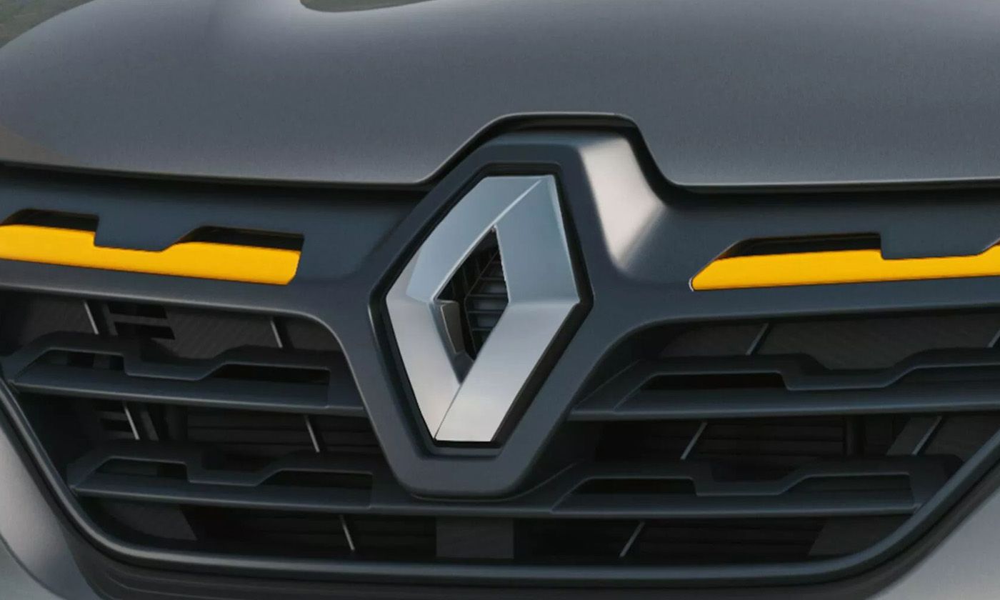 Close-up of a Renault diamond logo centered on the car’s dark front grille with yellow accent lighting on both sides of the grille edge.