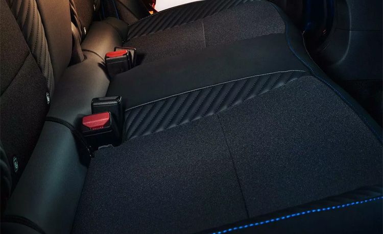 Rear car seat with two red seat belt buckles visible against dark fabric upholstery.
