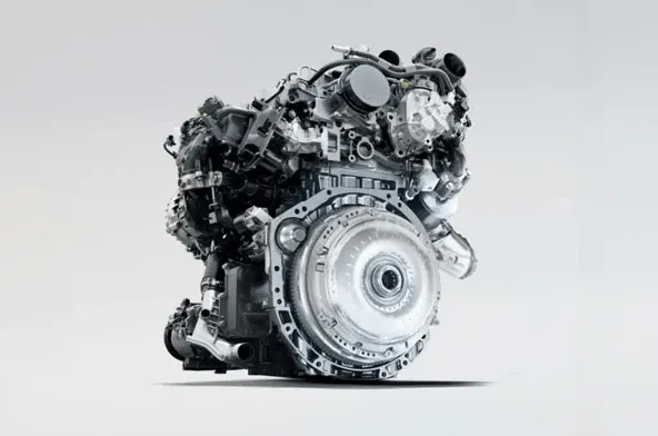 A modern car engine viewed from the side, showing a metallic silver crankcase and surrounding components against a light background.